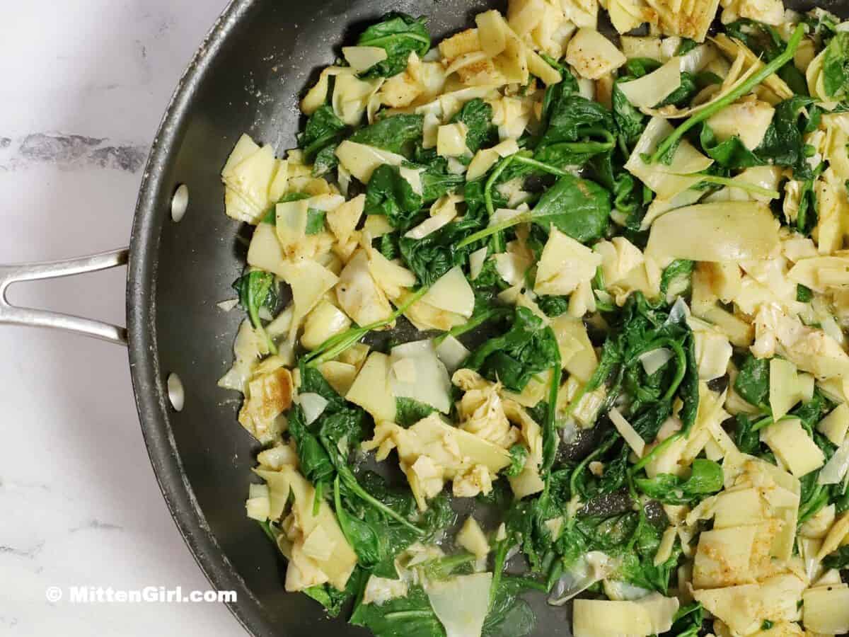 Spinach, artichoke hearts, and spices in a skillet. 