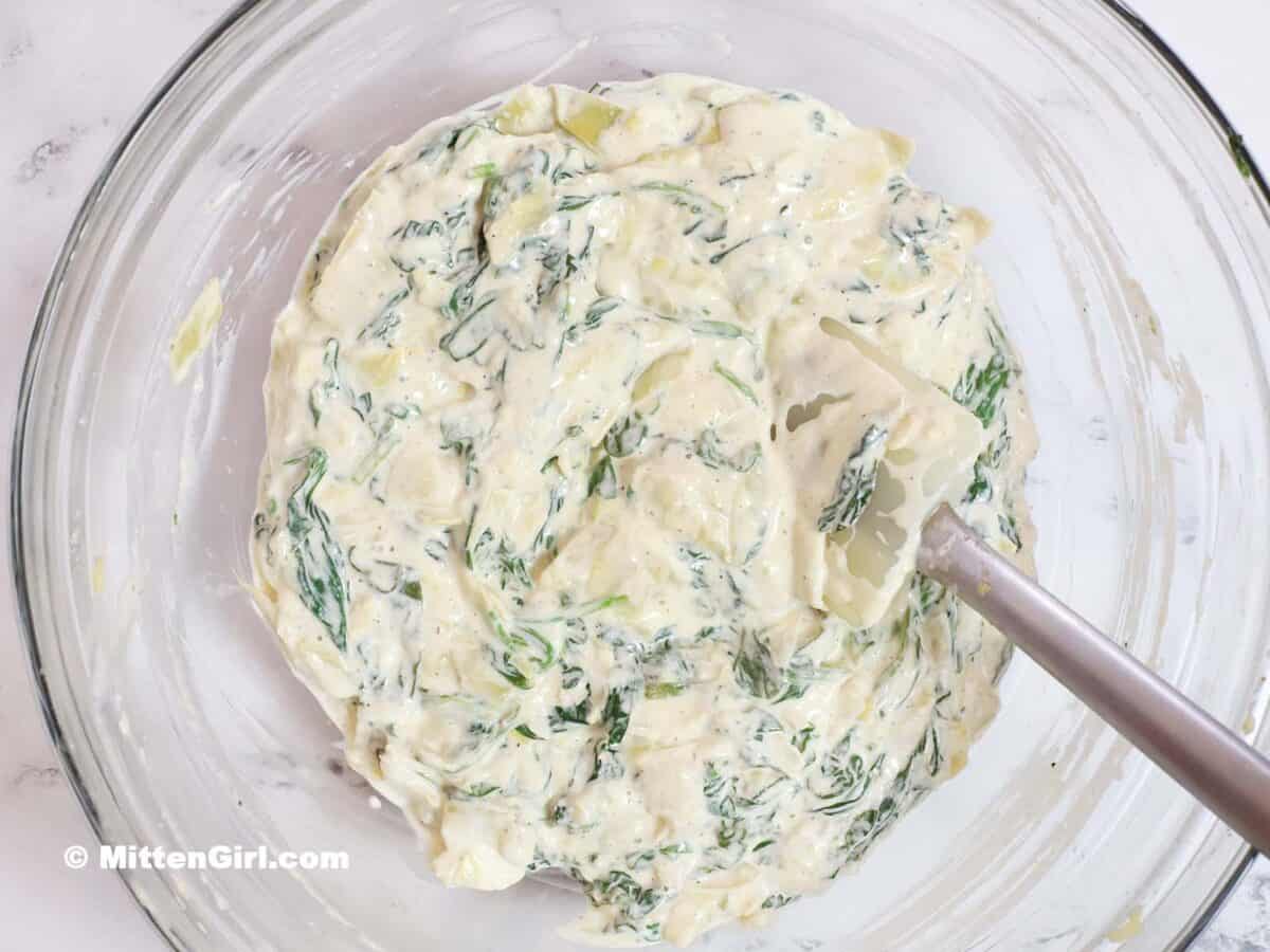 Spinach and artichoke mixture combined with three cheese mixture in a bowl