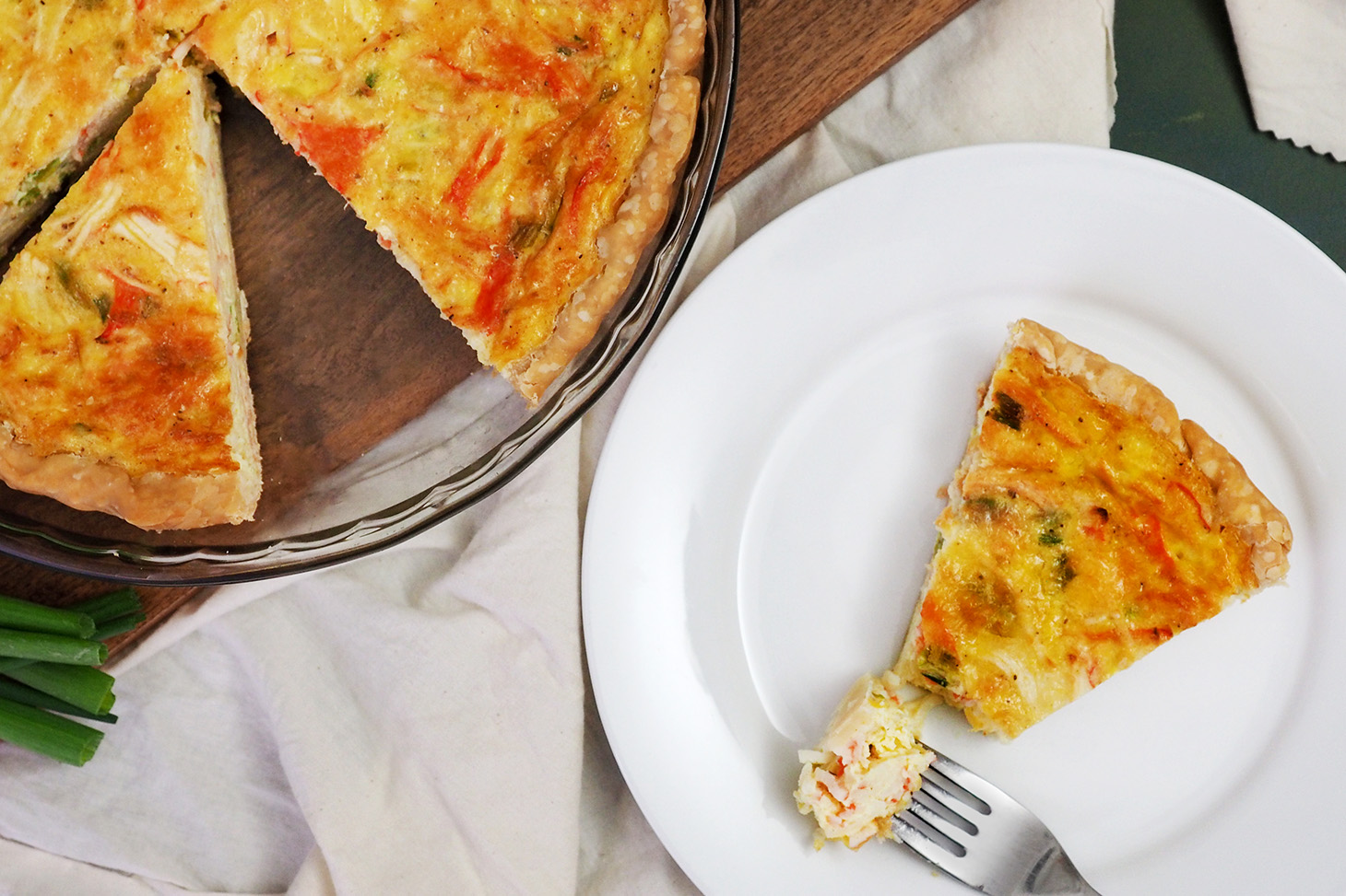 A white plate with a slice of crab quiche on it and a fork with a bite of quiche on it.