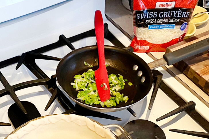 A skillet of sliced green onions on a stove with a red spatula sticking out of the pan.