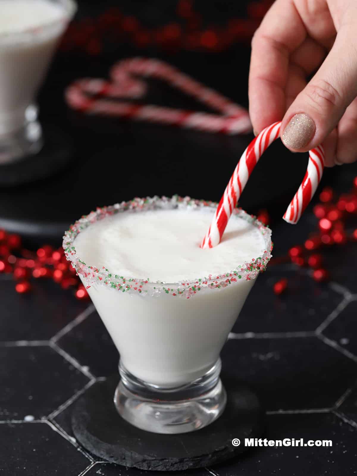 A hand garnishing a candy cane martini with a candy cane.