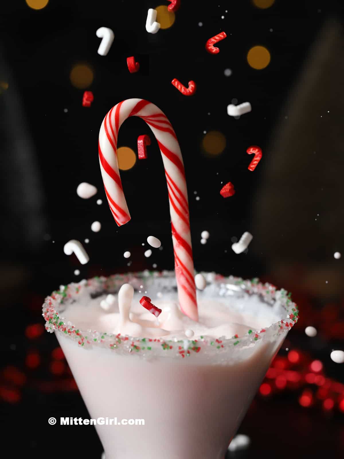 A candy cane and decorations splashing into a martini.