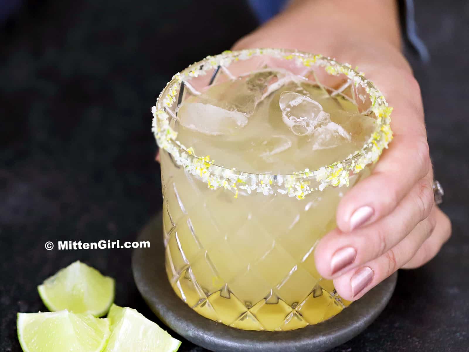 A hand picking up a glass of citrus margarita.