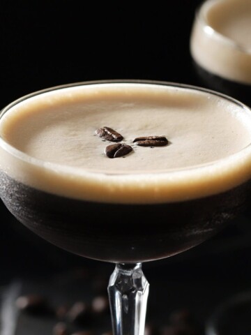 Two glasses filled with espresso martini with foam on top and garnished with 3 coffee beans.