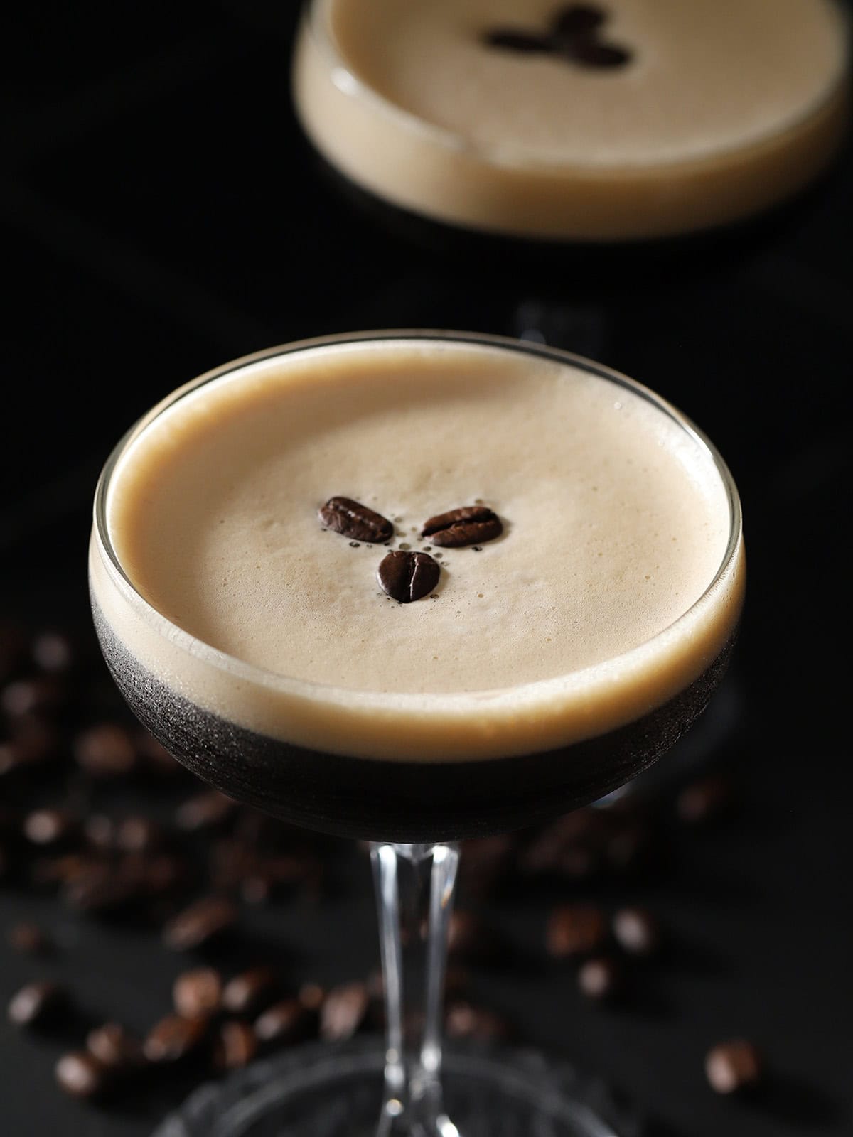 Two glasses filled with espresso martini with foam on top and garnished with 3 coffee beans.