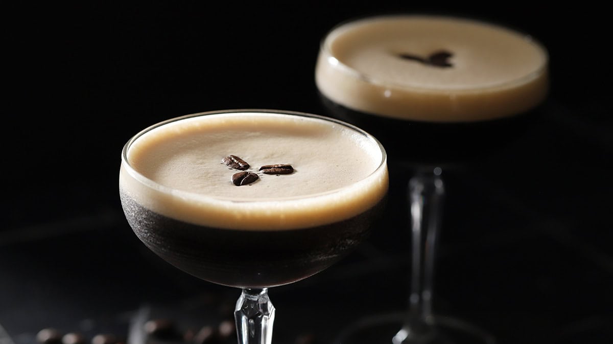 Two glasses filled with espresso martini with foam on top and garnished with 3 coffee beans.