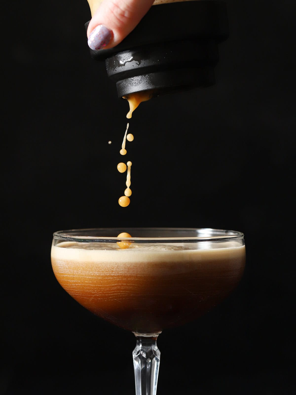 Espresso martini cocktail being poured from a cocktail shaker into a coupe glass.