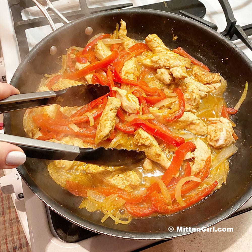 Sliced chicken cooking with onions, peppers, and spices for using in fajitas