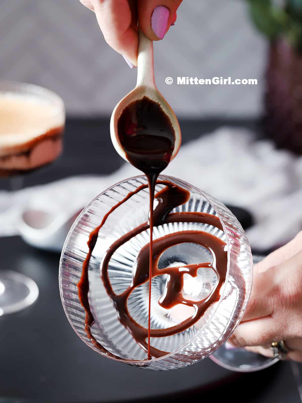 A spoon drizzling chocolate sauce into a glass.