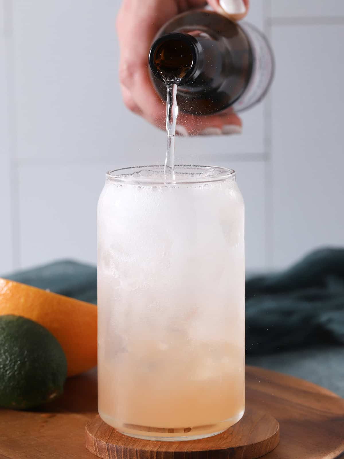 A hand pouring sparkling water from a brown bottle into a glass of Paloma cocktail. 