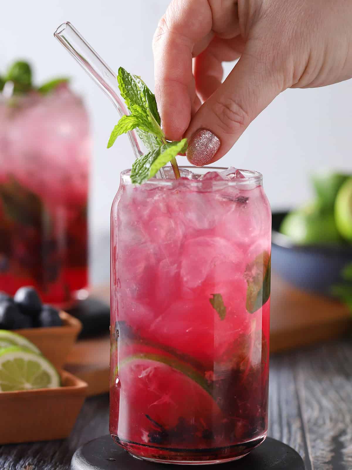 A hand placing a sprig of fresh mint into a glass of blueberry mojito. 