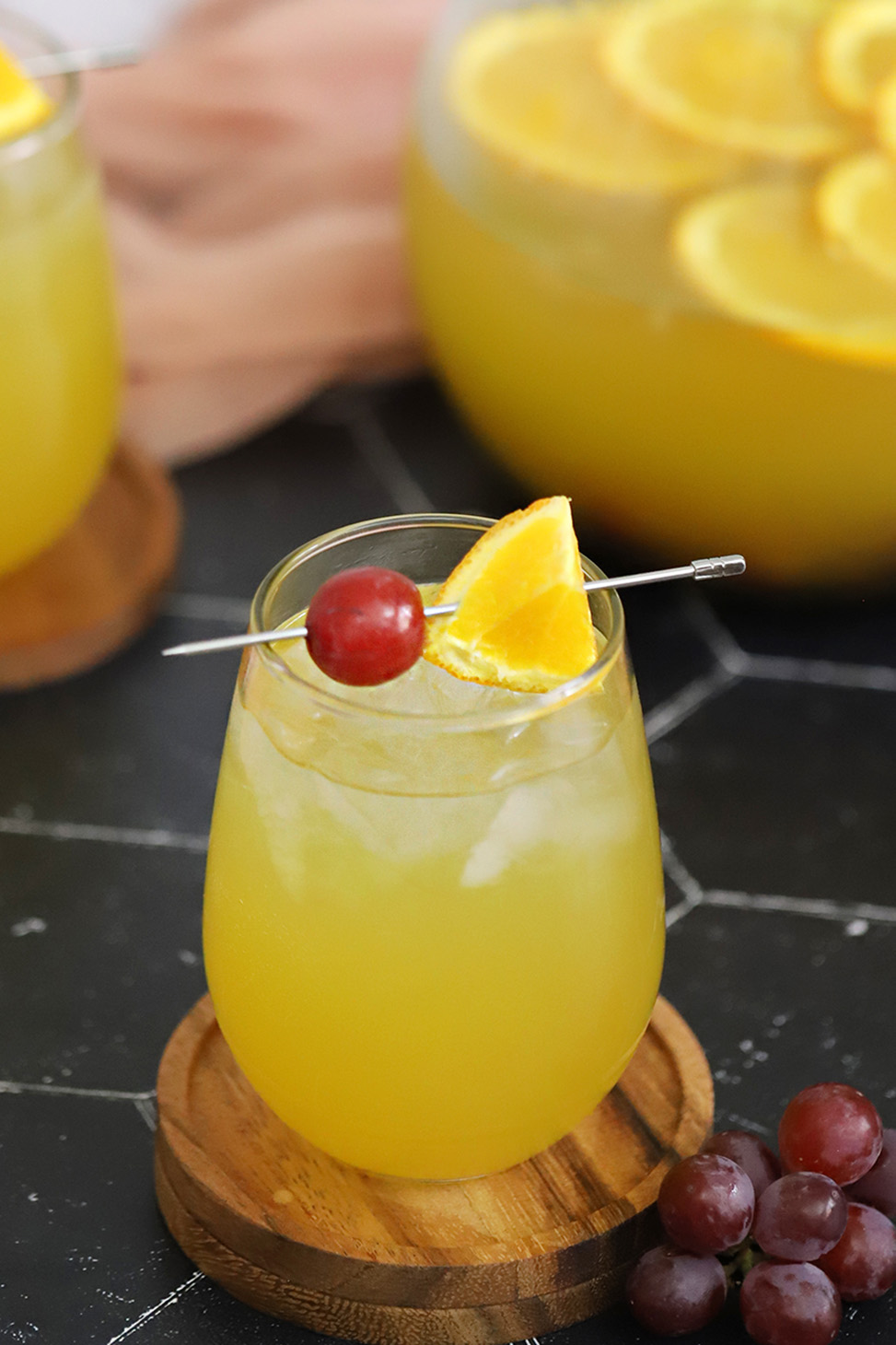 A glass of white wine sangria garnished with a red grape and piece of orange on a silver cocktail pick.