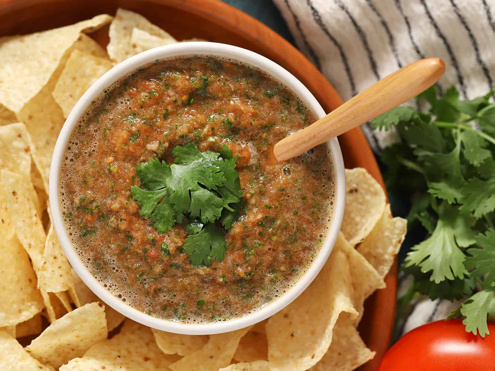 Looking down at a bowl of salsa with a spoon in it, surrounded by tortilla chips.