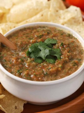 A bowl of salsa with a spoon in it, surrounded by tortilla chips.