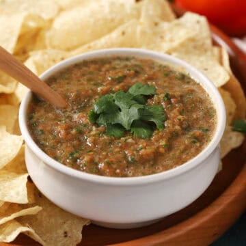 A bowl of salsa with a spoon in it, surrounded by tortilla chips.