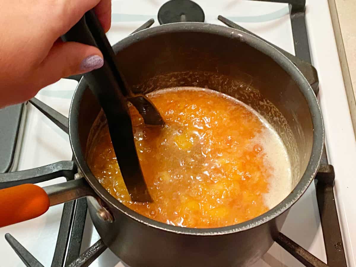 Mashing cooked peaches in a pot on the stove