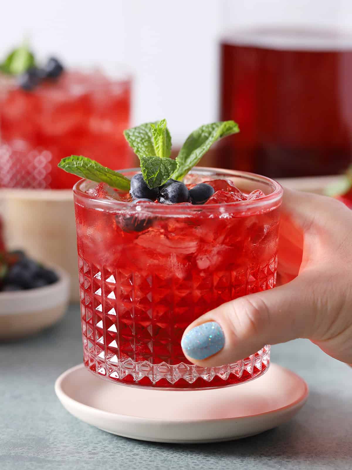 A hand picking up a glass of large batch pitcher drink.