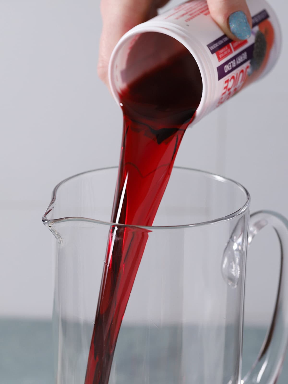 A thawed can of juice concentrate being poured into a pitcher. 