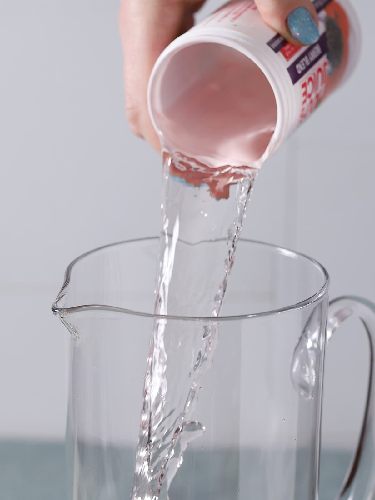 A hand pouring vodka from a juice concentrate can into a pitcher. 
