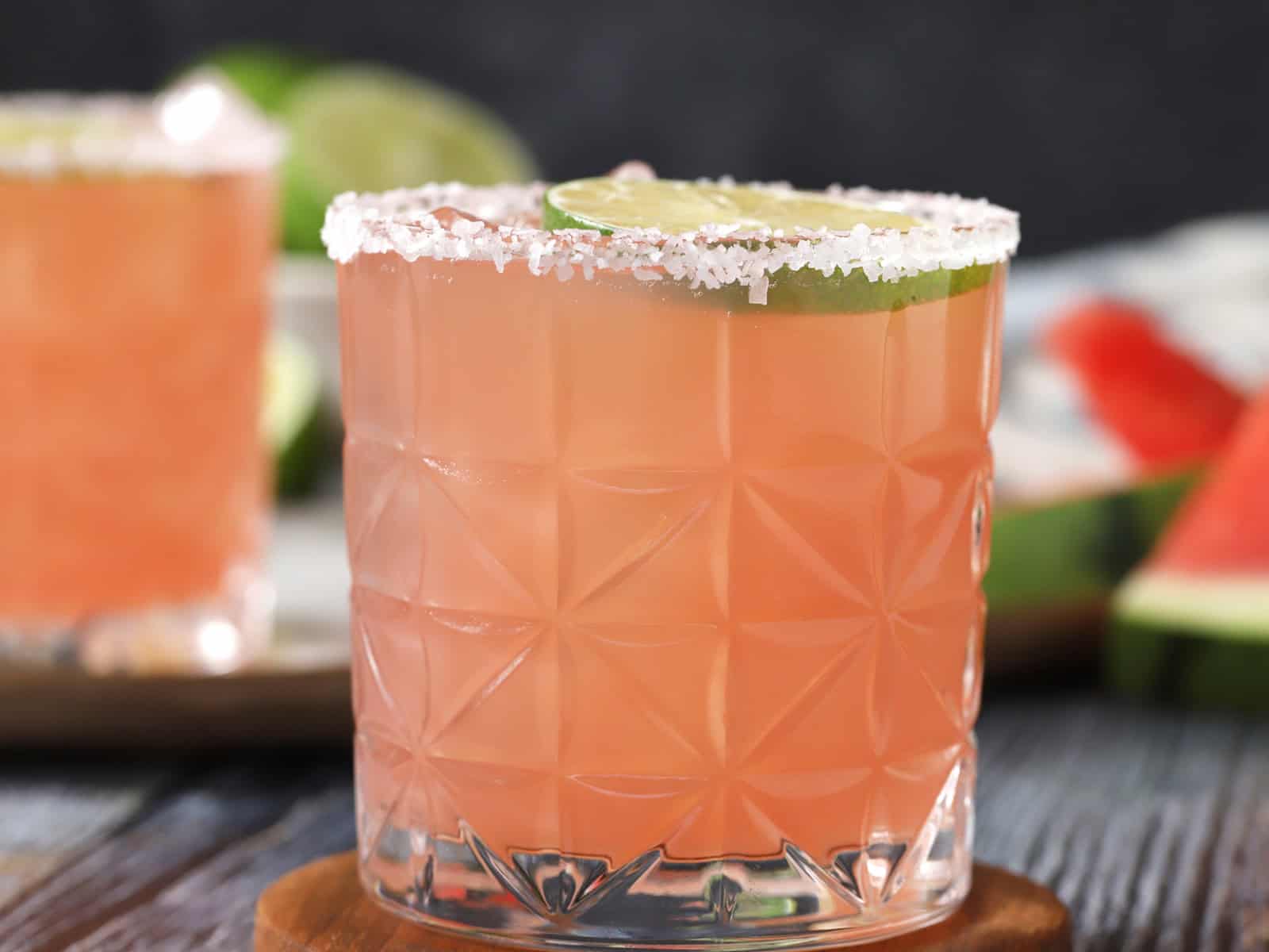 A rocks glass filled with watermelon margarita, garnished with fresh lime and watermelon slices.