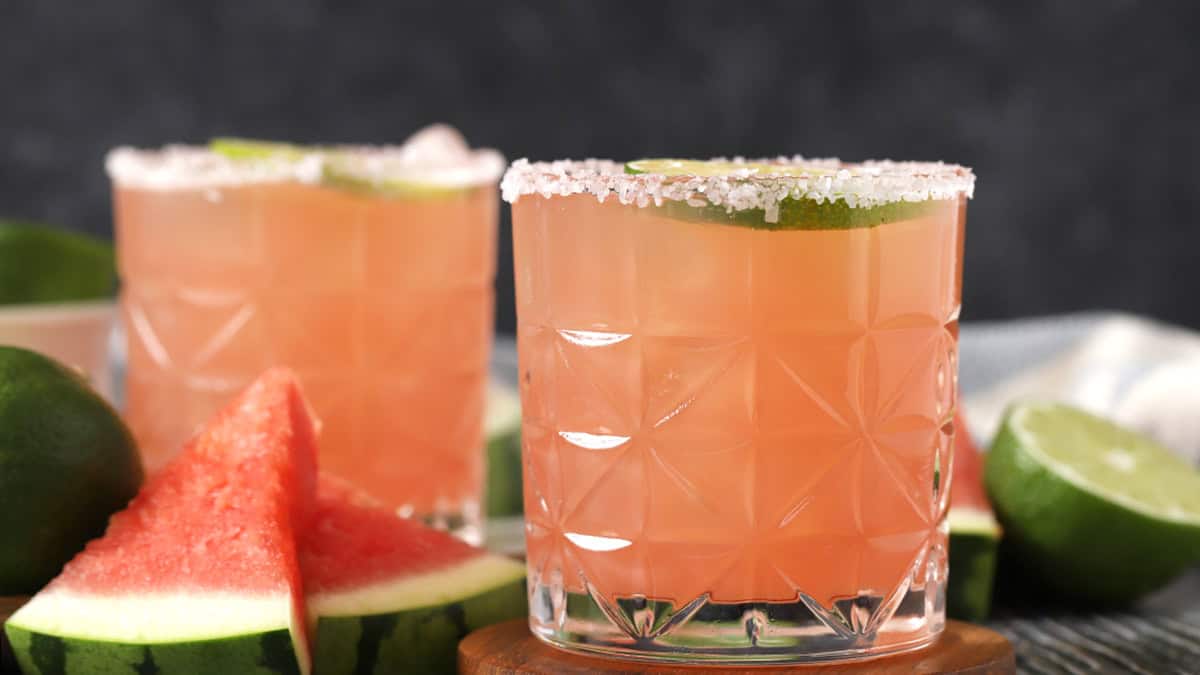 Two rocks glasses filled with watermelon margaritas, garnished with fresh lime and watermelon slices.