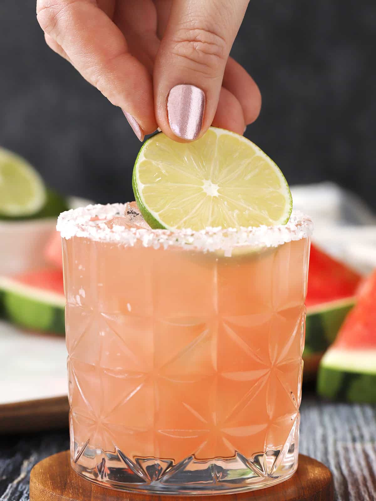 A hand placing a lime wheel onto a glass filled with watermelon margarita.