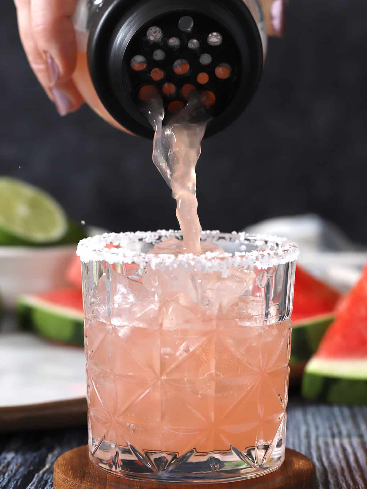 A hand pouring watermelon margarita from a shaker into a glass. 