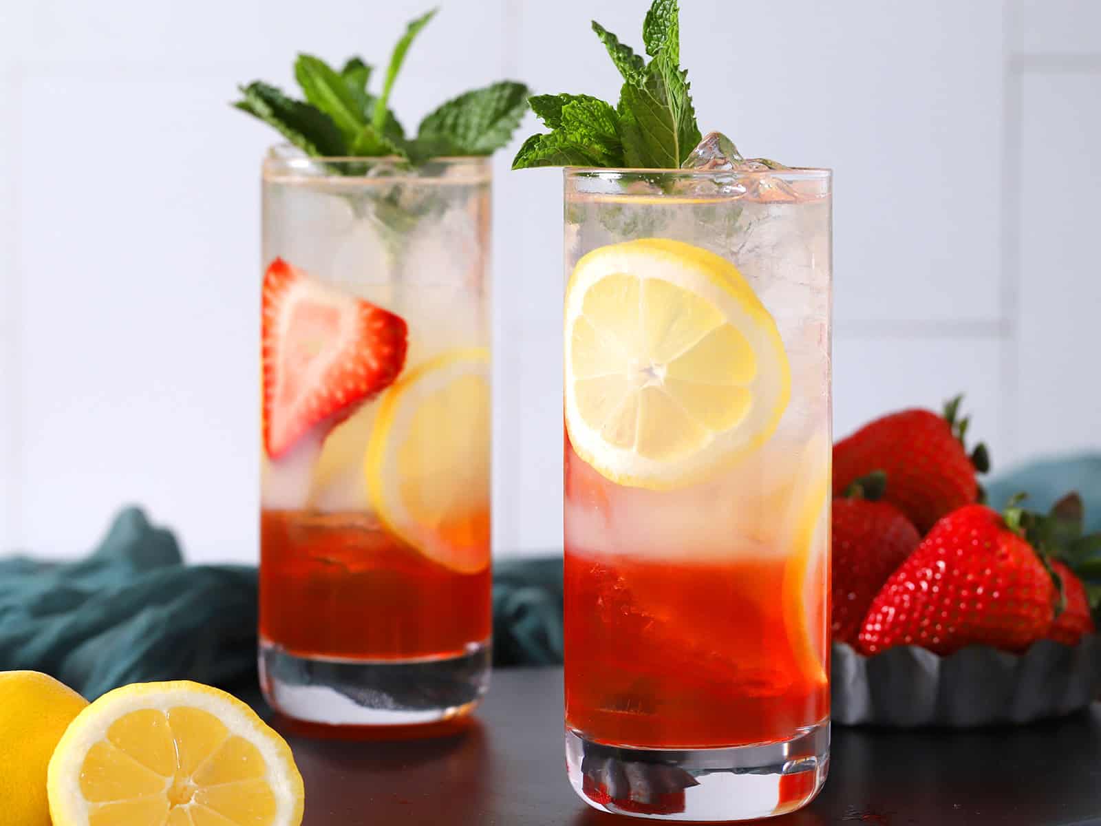 Two glasses of layered strawberry lemonade cocktail garnished with mint.