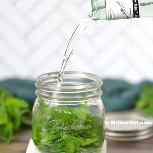 Rum being poured into a jar filled with mint and lime.