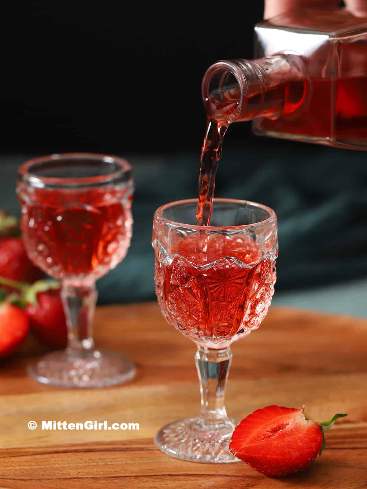 Strawberry infused vodka being poured into a small glass.