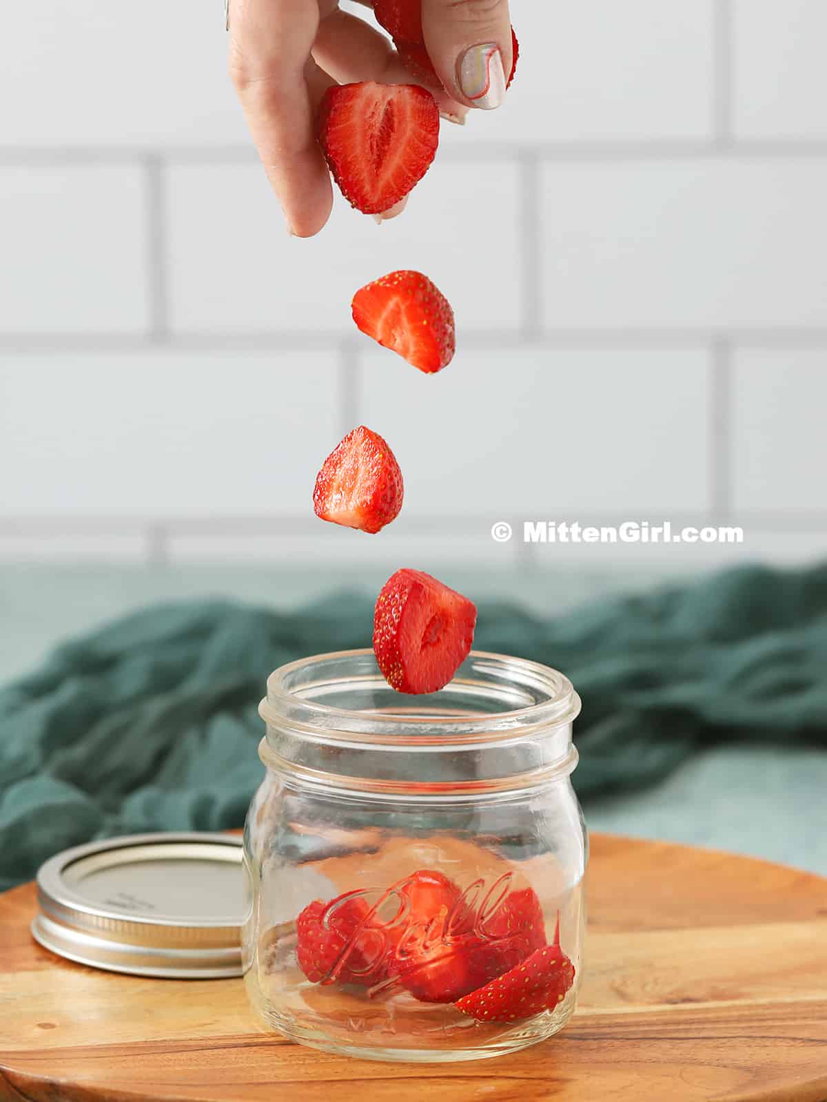 Strawberries being dropped into a mason jar. 