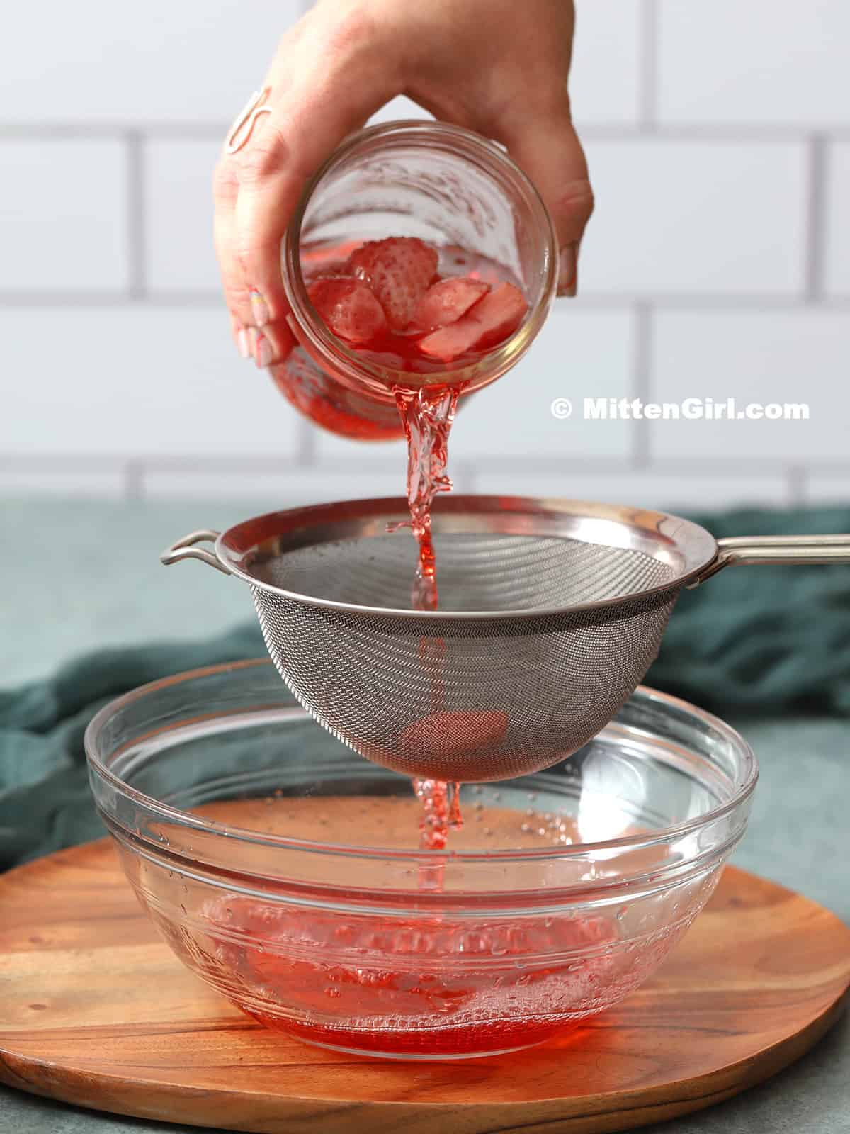 Strawberry infused vodka being strained through a fine mesh sieve.