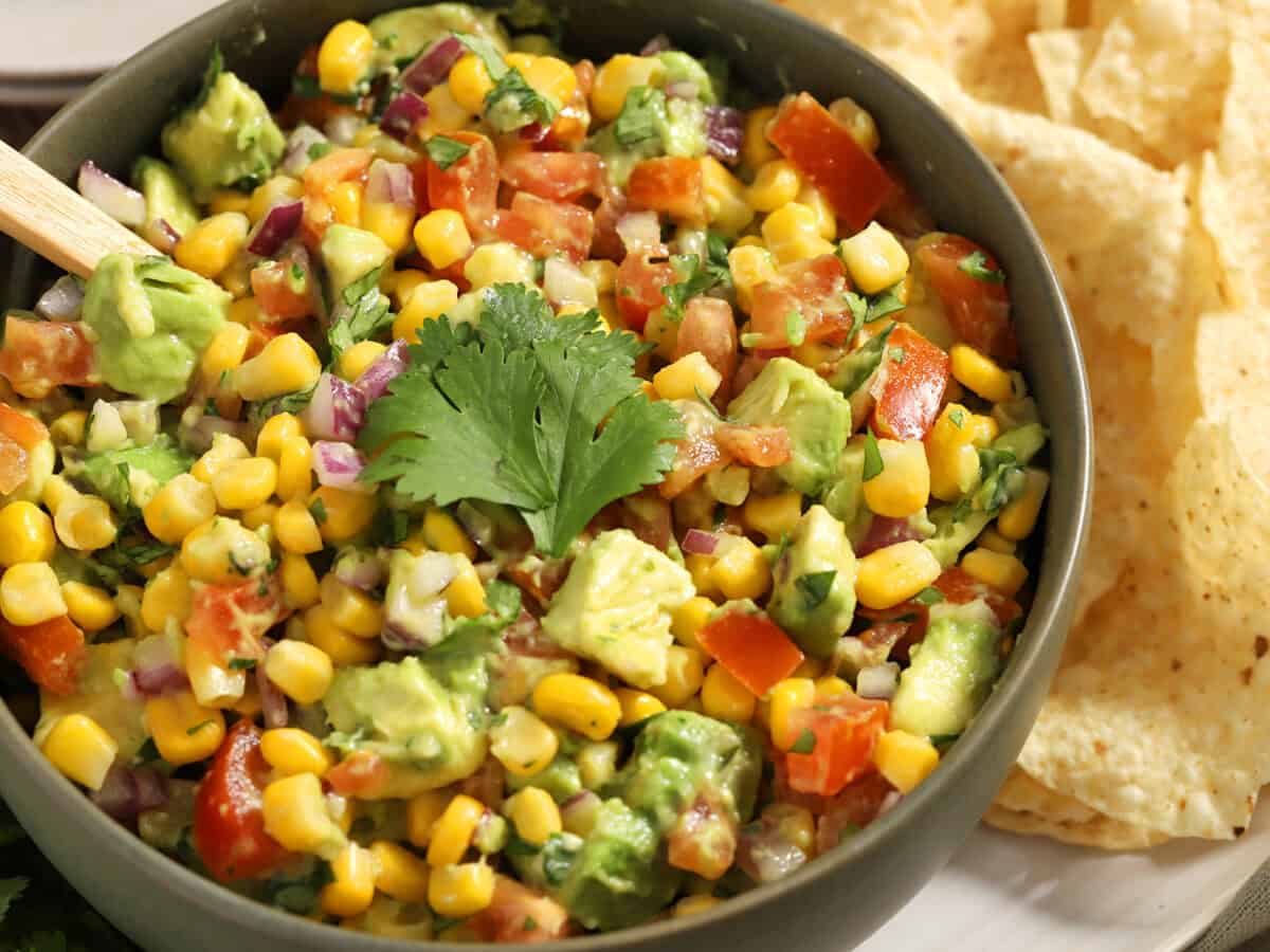 A bowl of avocado and corn salsa next to a pile of tortilla chips.