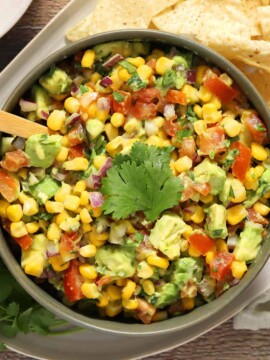 A bowl of avocado and corn salsa next to a pile of tortilla chips.