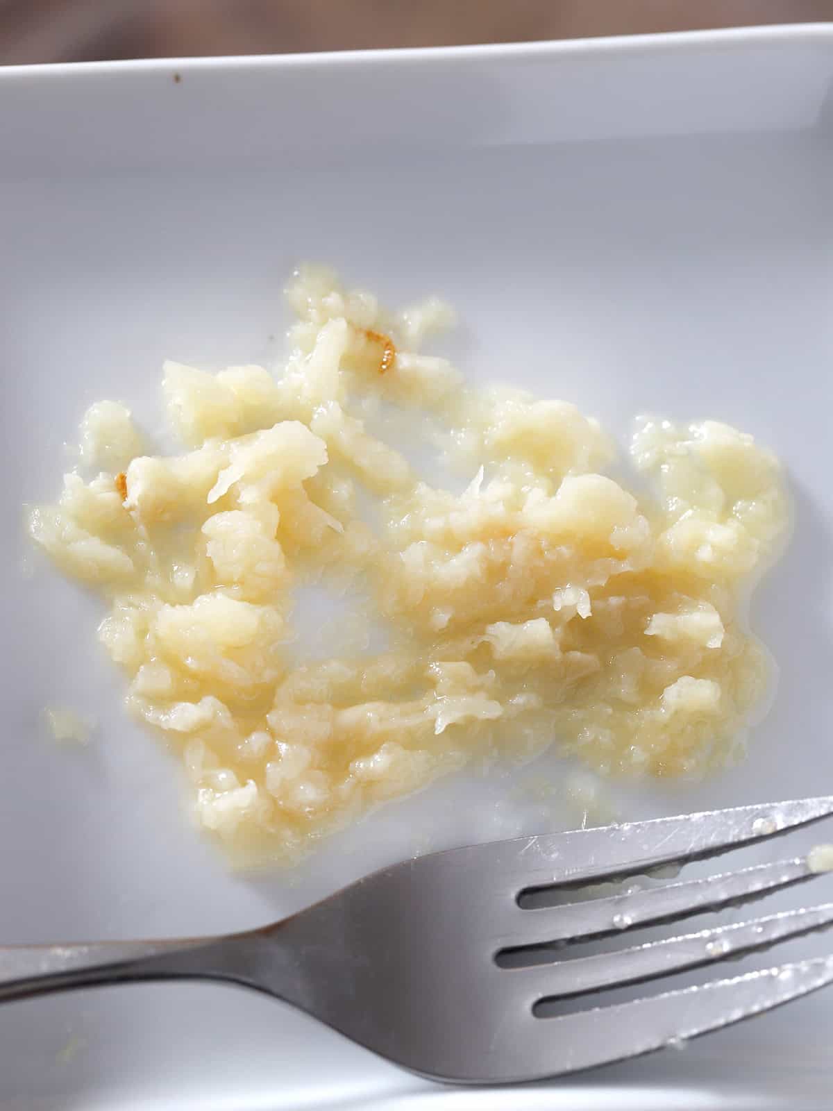 Roasted garlic mashed on a small plate, with a fork.