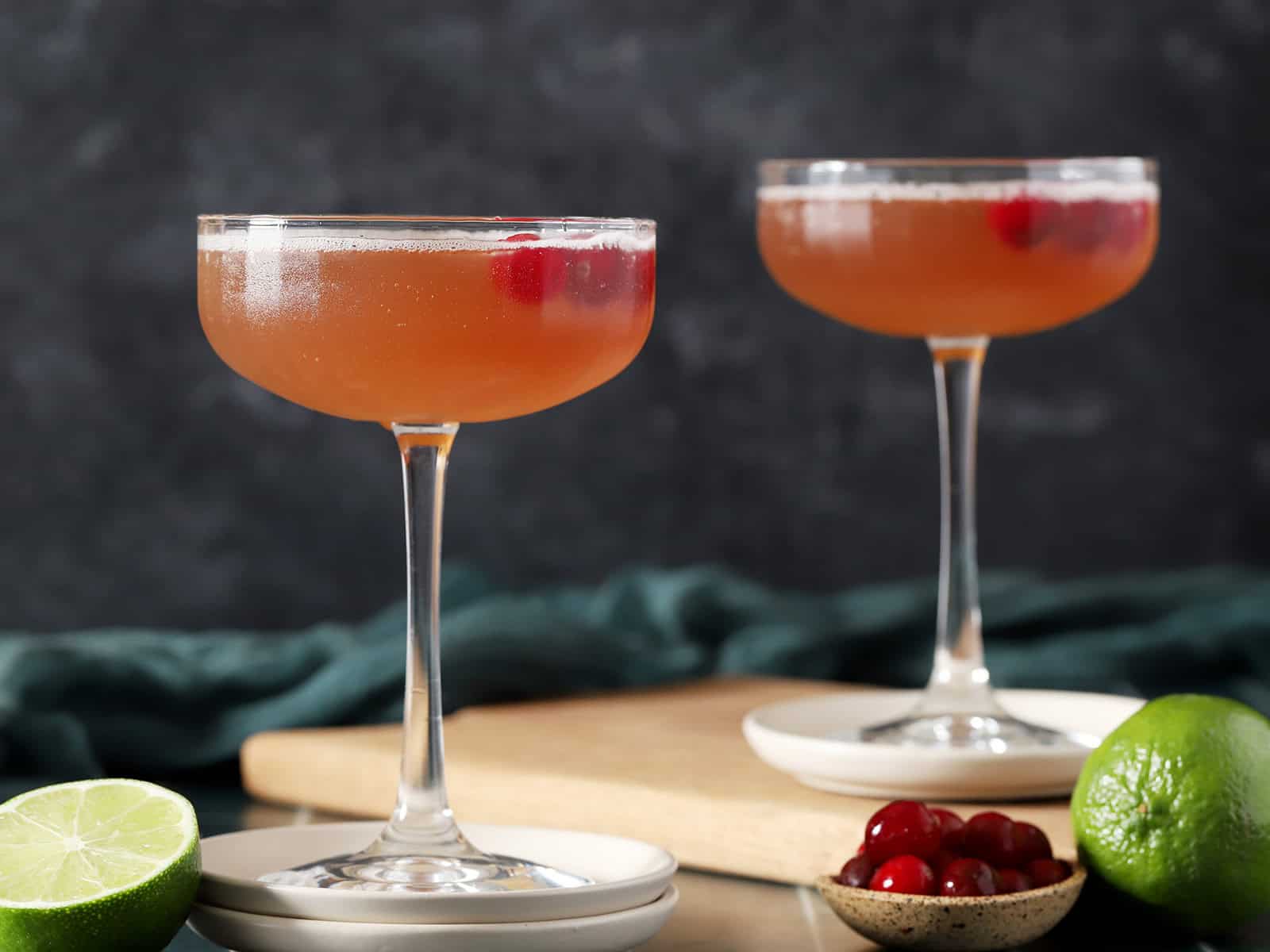 Two coupe glasses filled with Cosmos, garnished with cranberries and a lime slice.