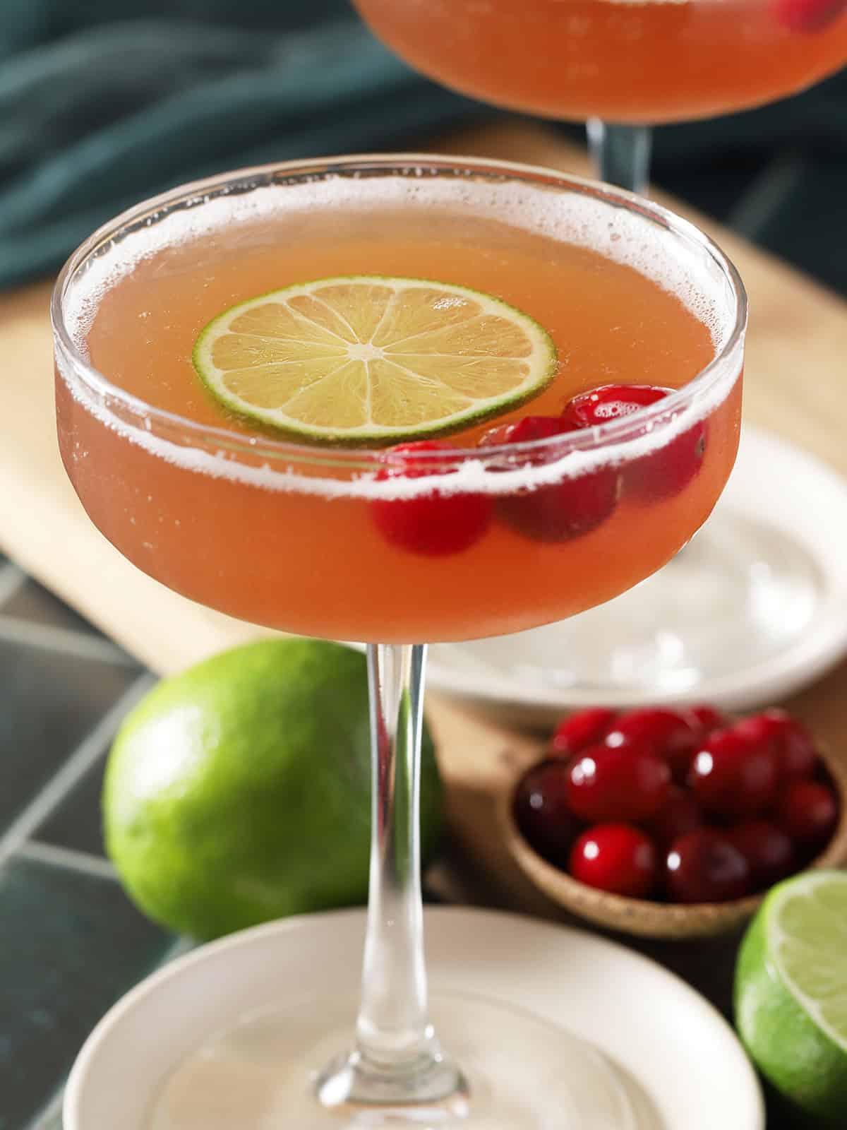 A coupe glass filled with Cosmos, garnished with cranberries and a lime slice.