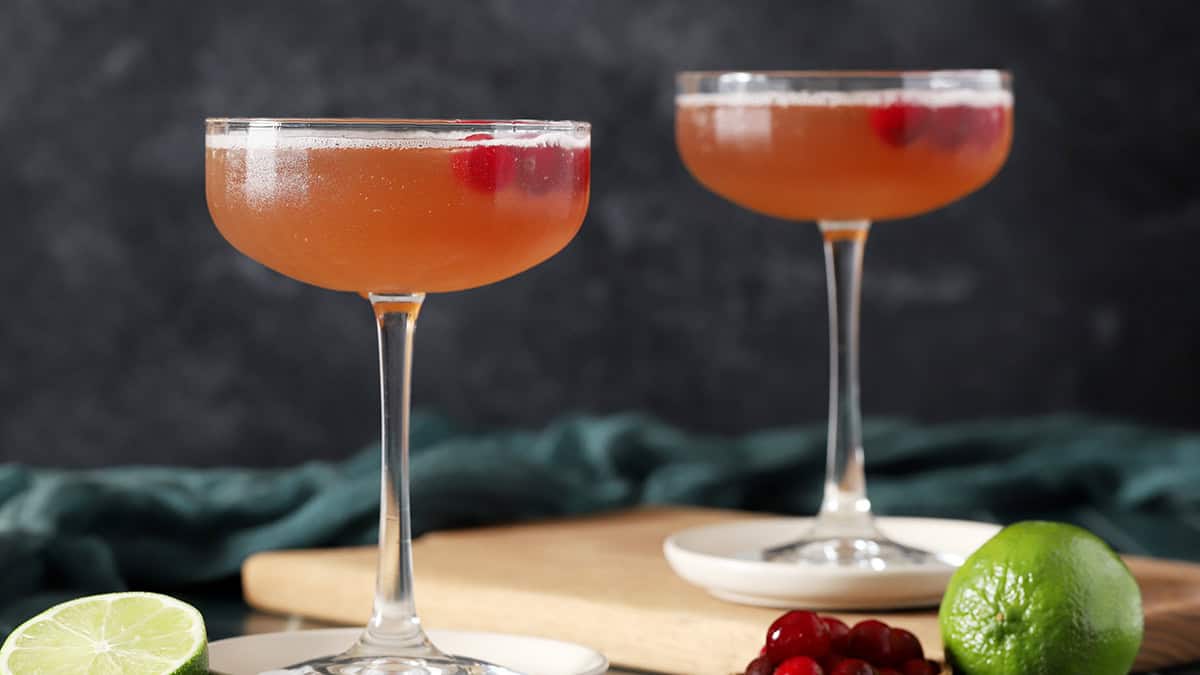 Two coupe glasses filled with Cosmos, garnished with cranberries and a lime slice.