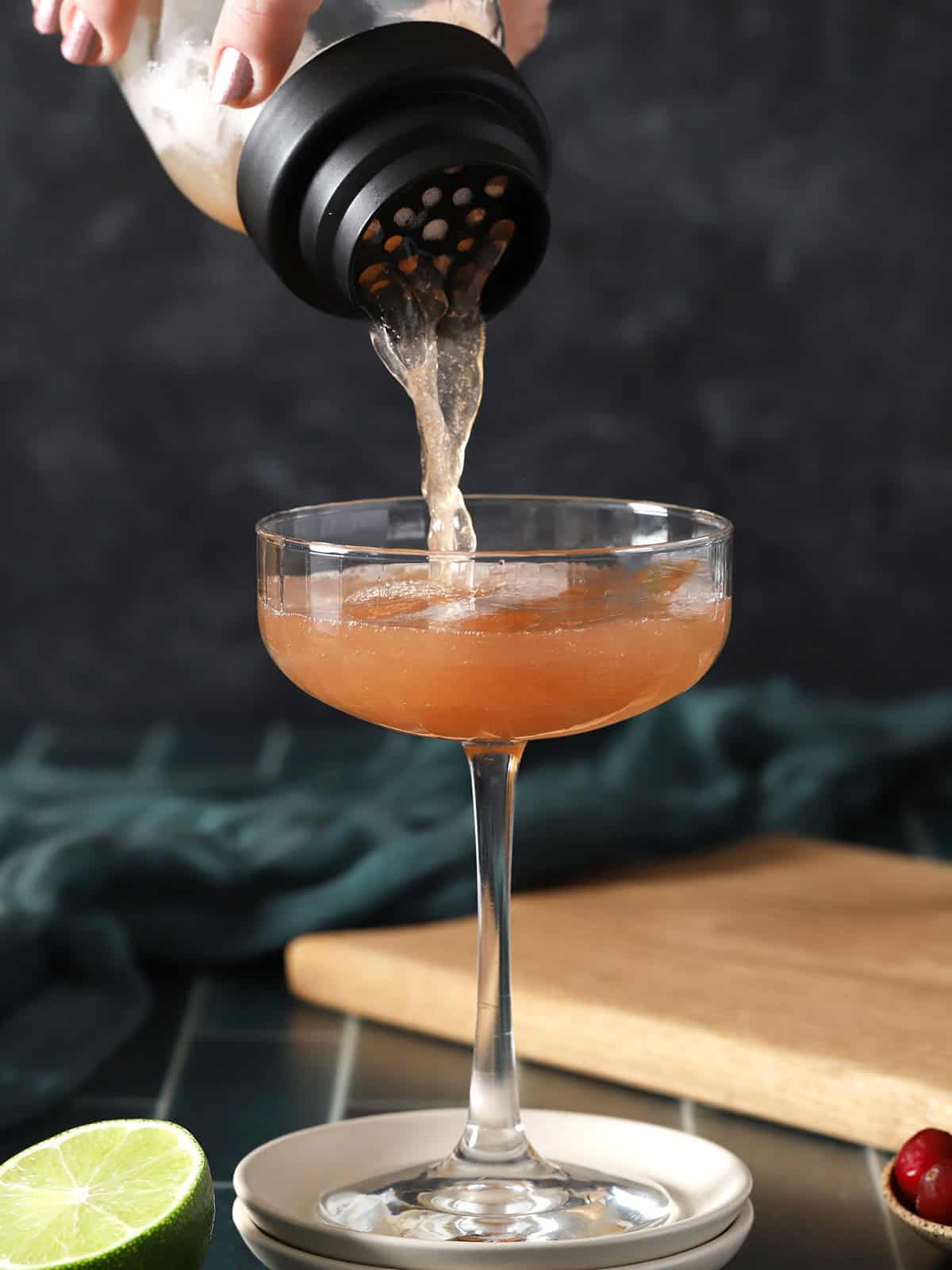 Cosmo cocktail being poured from a cocktail shaker into a coupe glass. 