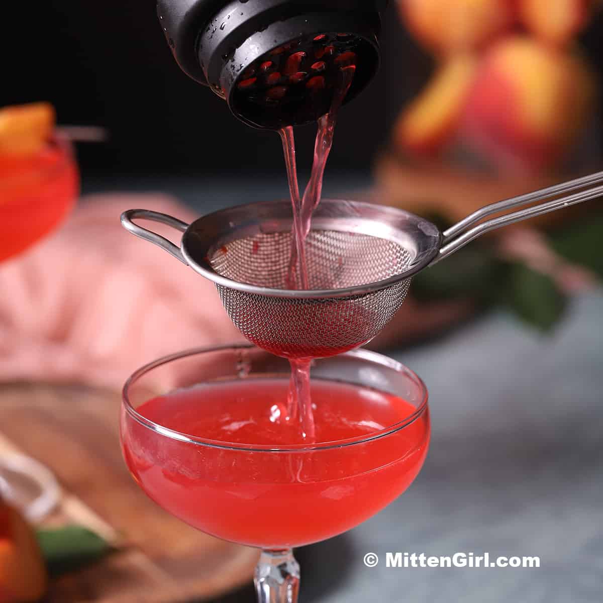 Raspberry Peach Martini being poured through a strainer into a cocktail glass.