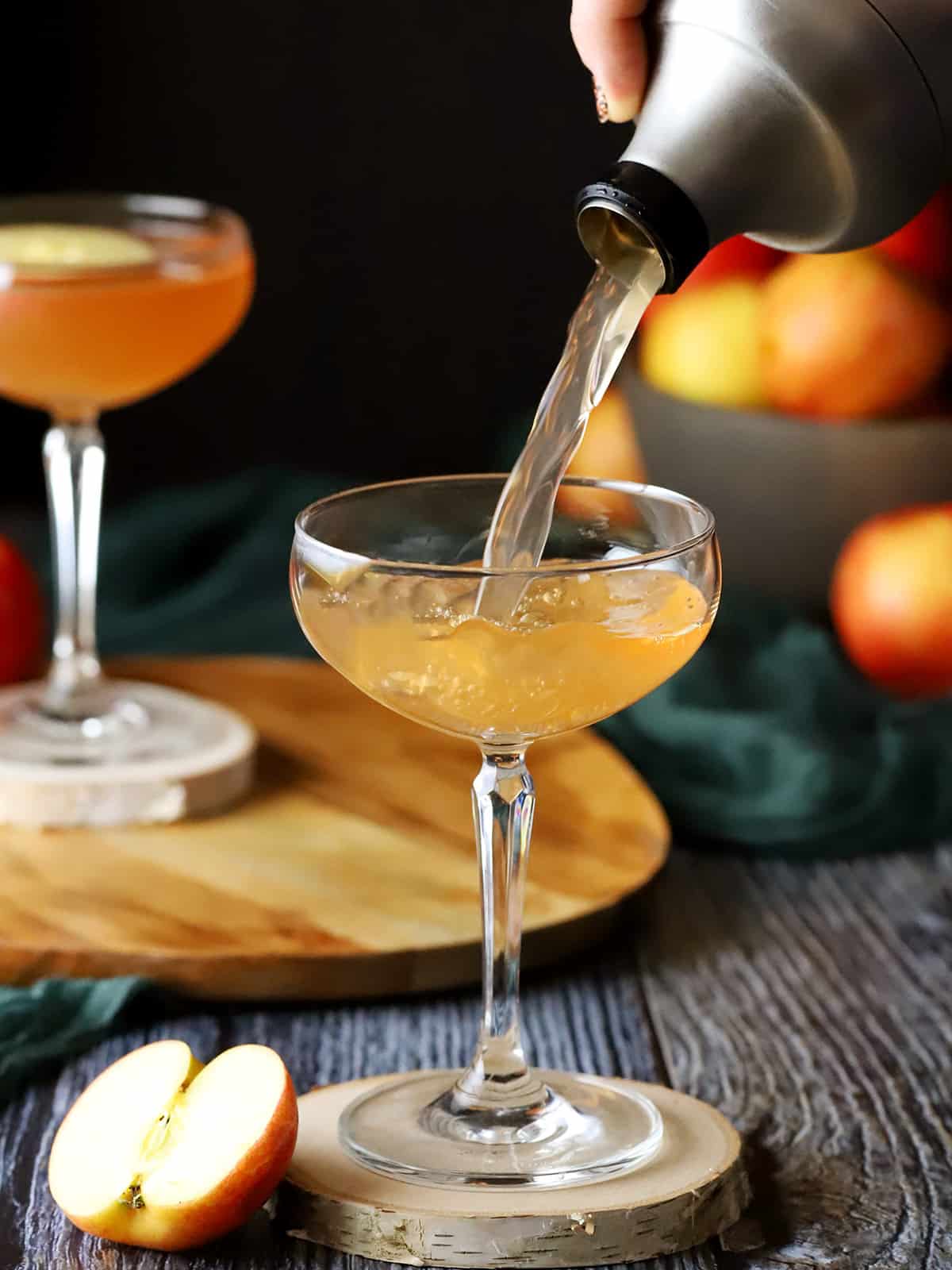 A hand pouring apple vodka cocktail into a coupe glass. 