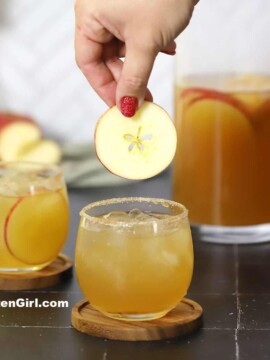 A hand placing an apple slice into a glass of sangria.