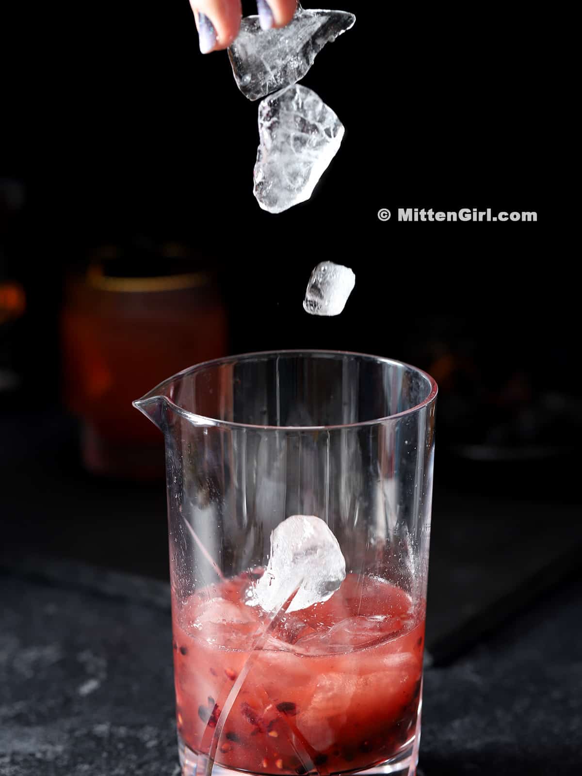 Ice falling into a mixing glass with cocktail.