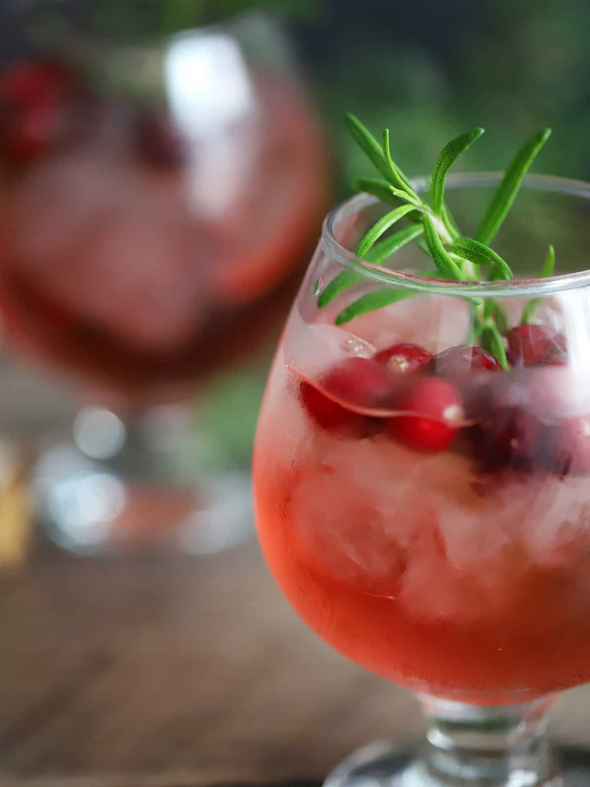 A glass of cranberry Christmas Cocktail garnished with rosemary. 