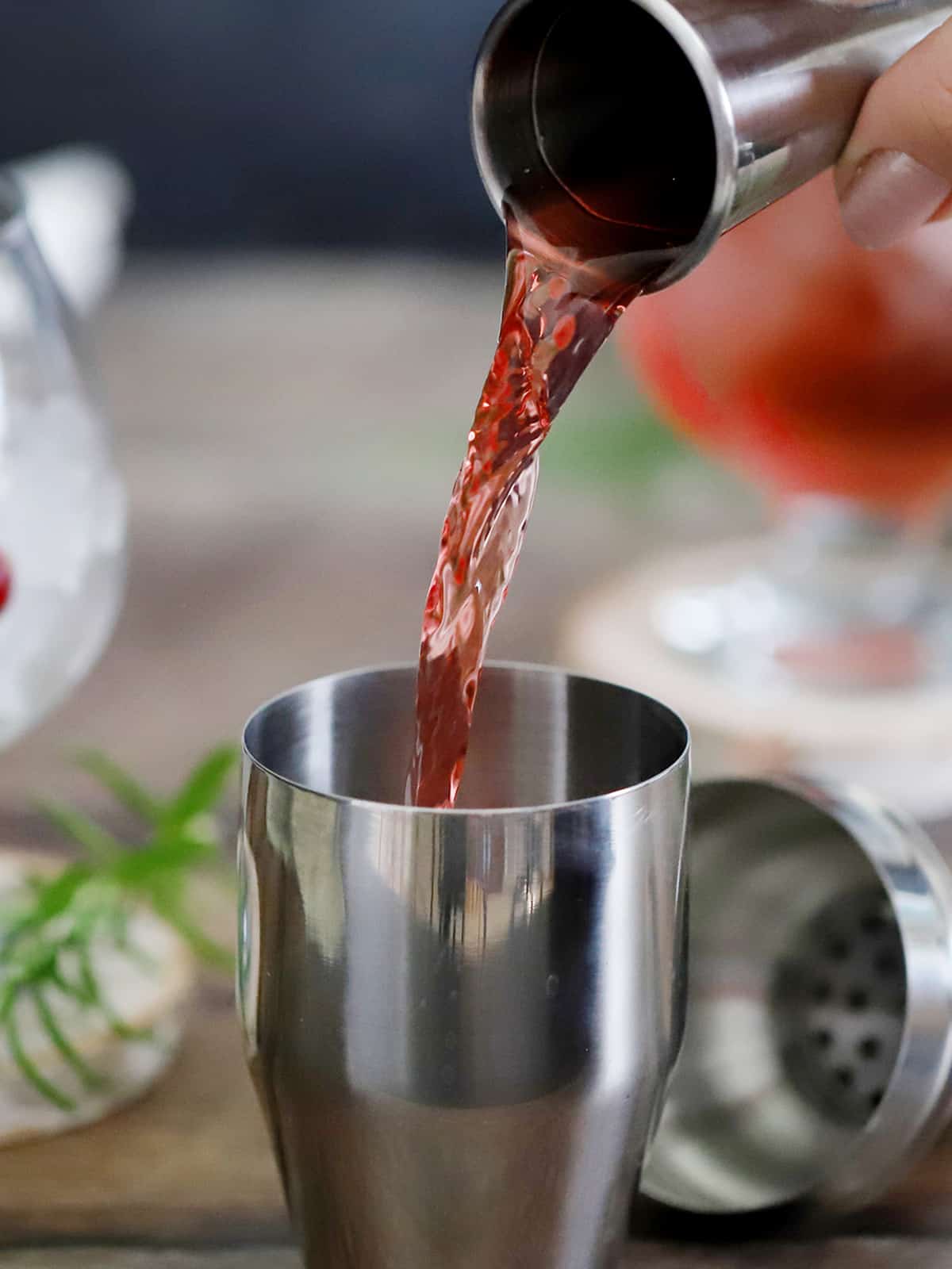 Cranberry juice being poured into a cocktail shaker. 