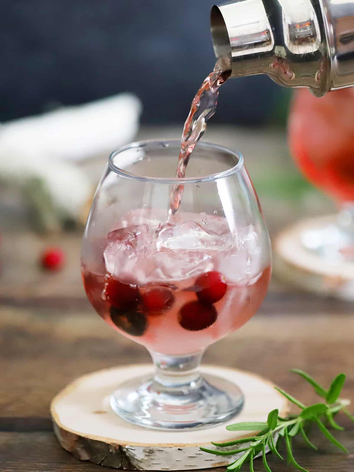 Cranberry Gin Cocktail being poured from a cocktail shaker into a glass filled with ice. 