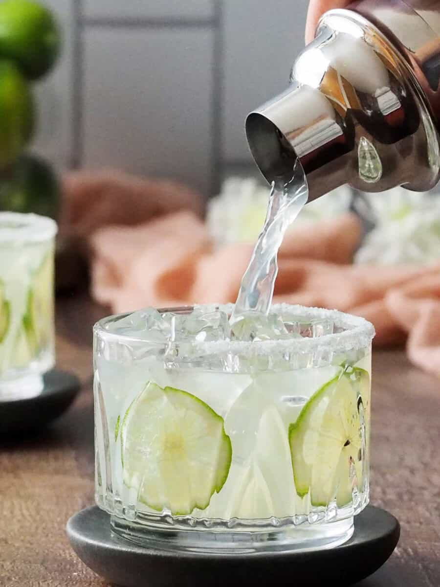 Elderflower margarita being poured into a prepared rocks glass.