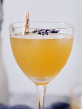 A glass filled with lavender bee's knees cocktails garnished with sprigs of lavender.