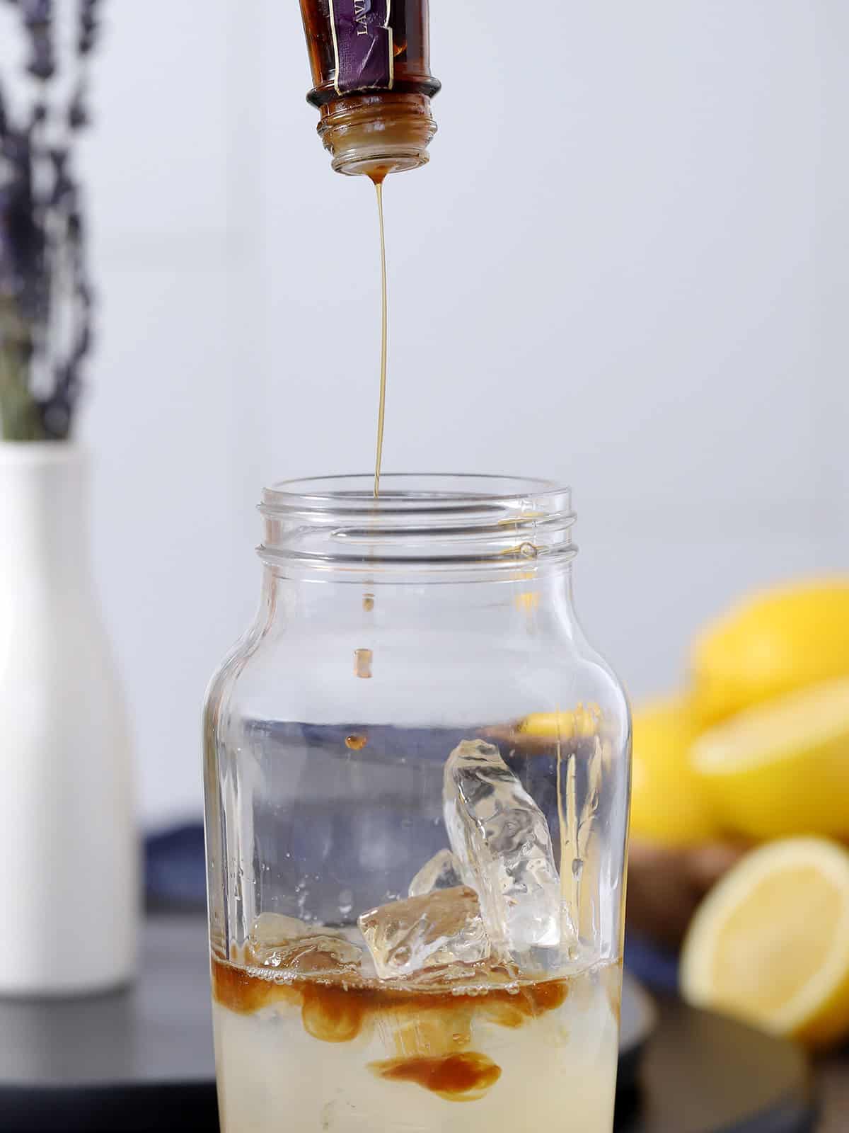 Dashes of lavender bitters running from an upside down bottle into a cocktail shaker.