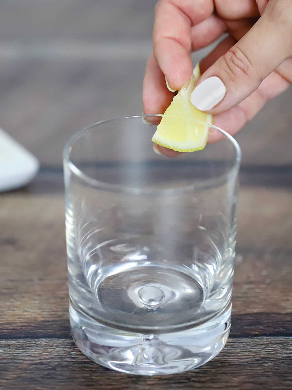 A hand running a slice of lime around the rim of a glass.